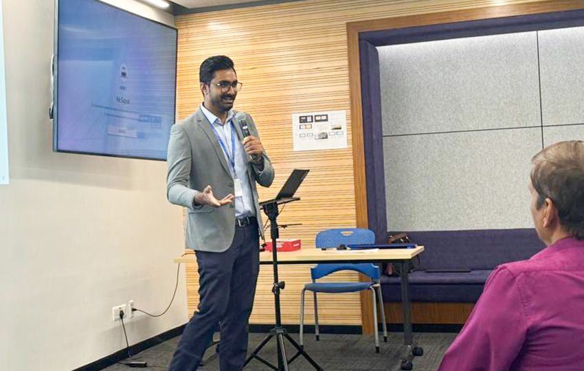 Man in a sport coat speaking into a microphone in a conference room.