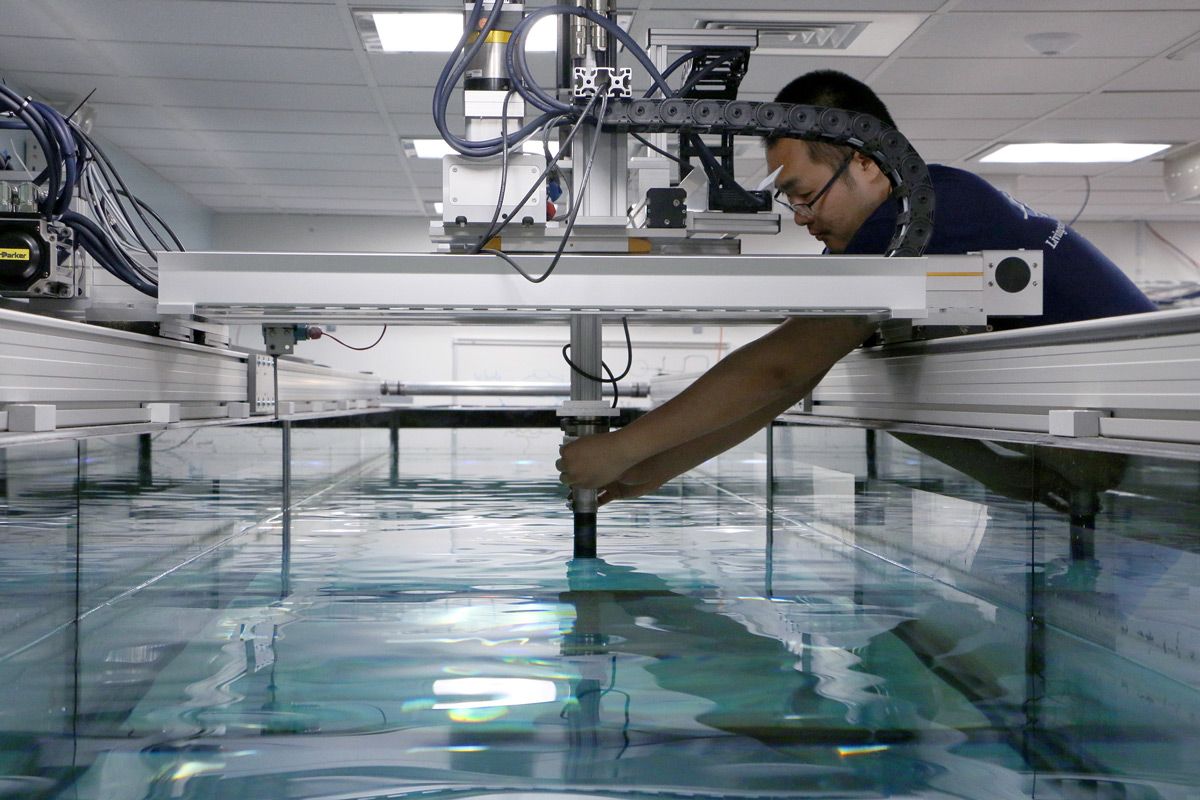 Dr. Fan leans over the edge of the tank to adjust the robot. 