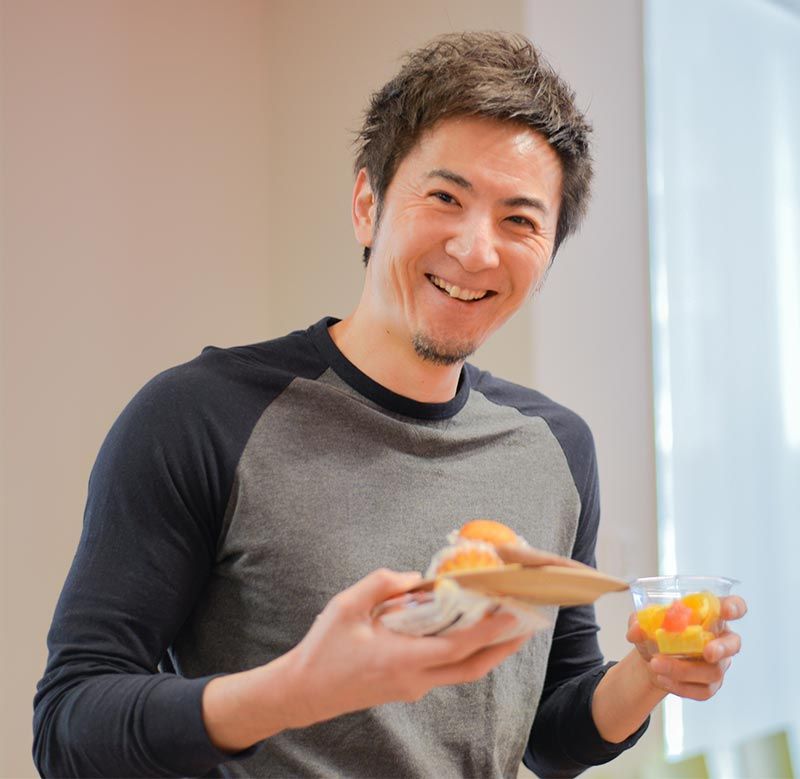 Smiling staff member holding fruit and baked goods from the breakfast buffet.