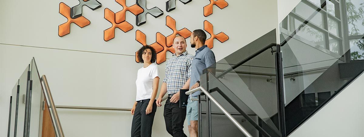 Three people walking down open stairway with modern design. 