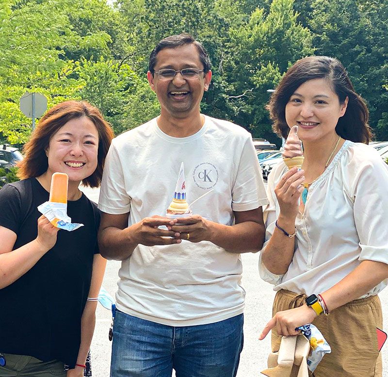 Three people posing outside with ice cream cones and other frozen treats.