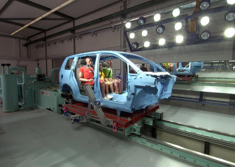 Three crash test dummies in back seat of automobile chassis with doors and front assembly removed. 