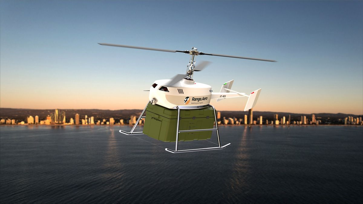 An autonomous helicopter flying over water near a city delivers a large crate.
