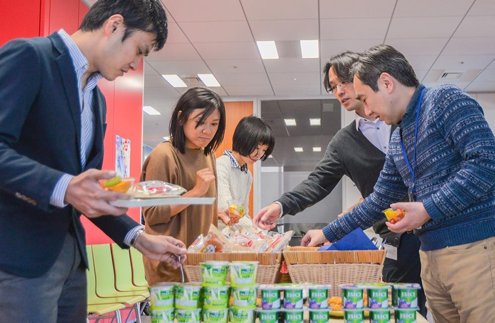 Five staff members getting fruit, yogurt, and other breakfast items from a buffet.