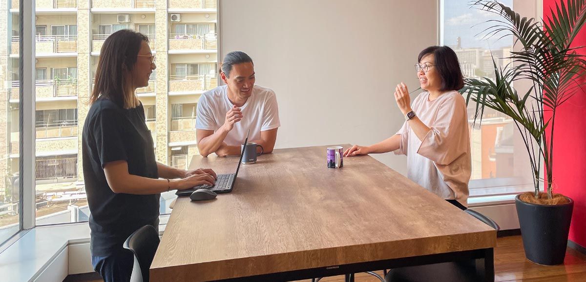 Three staff members standing around a high table chatting. One has a laptop open.