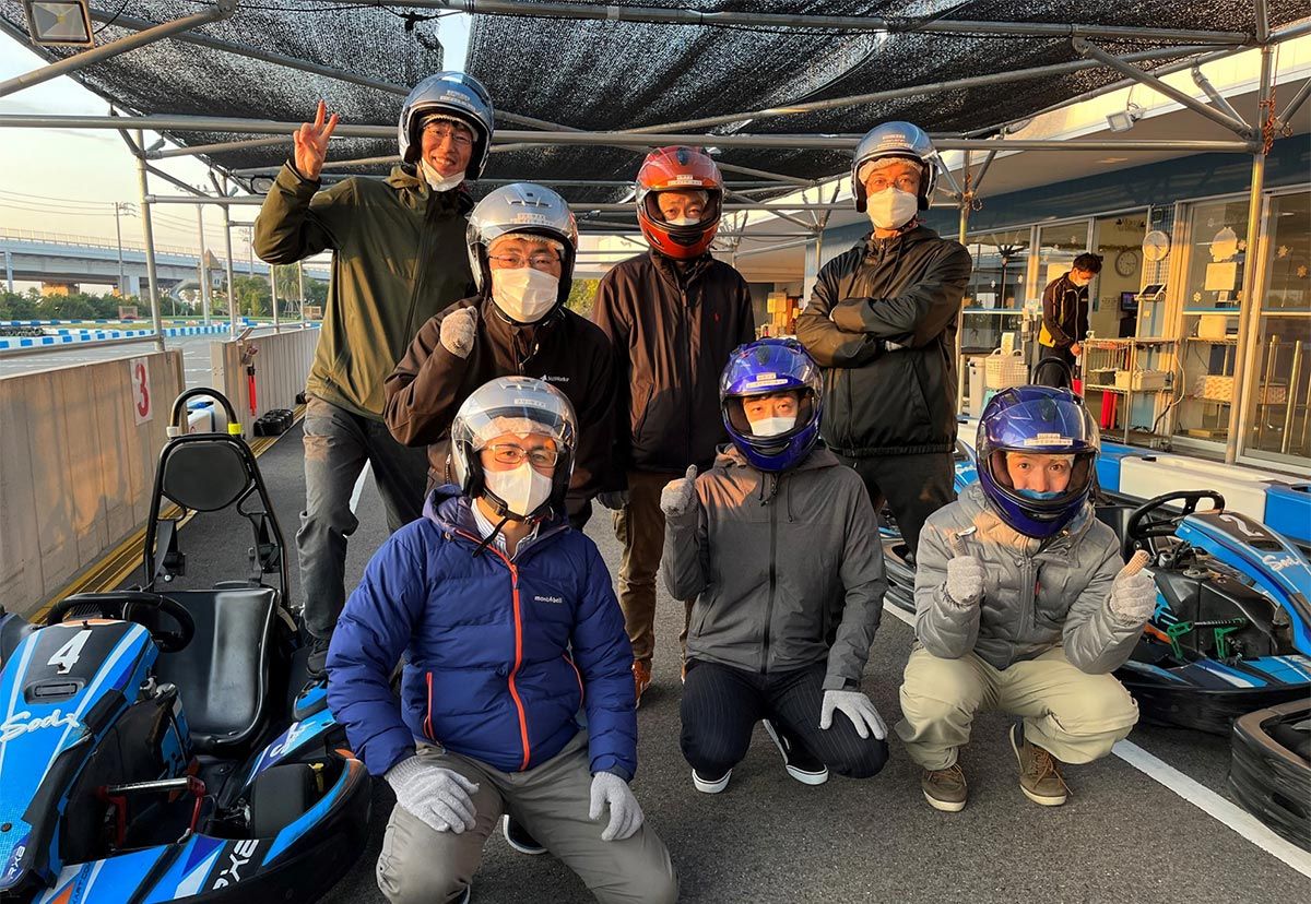Group photo of seven staff members in helmets at a team outing at a racetrack.