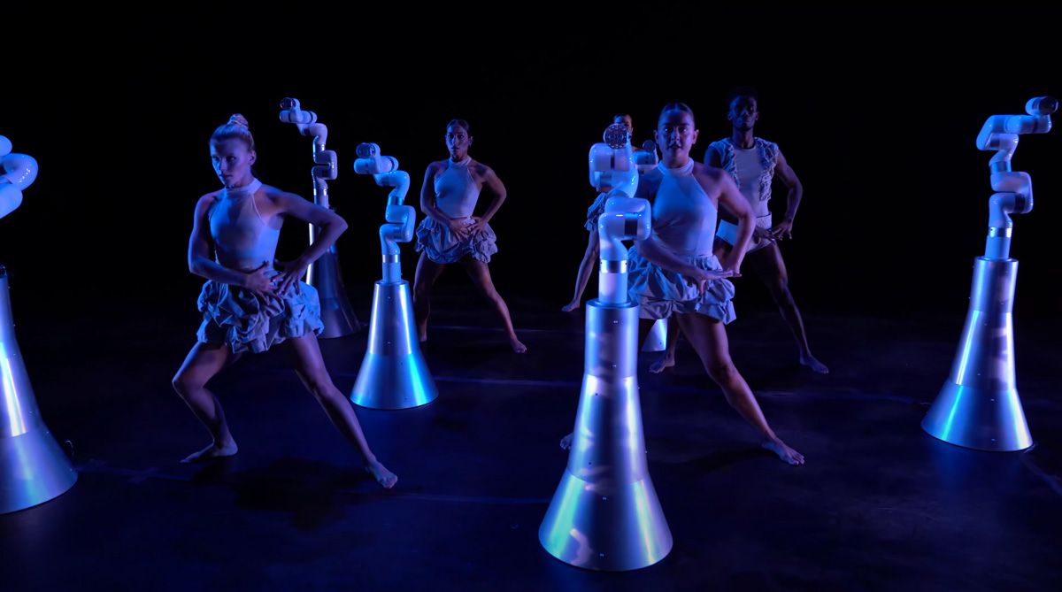 Six dancers with six robots performing on stage. 