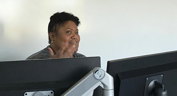 Louvere Walker-Hannon sitting at a desk with two monitors, while speaking and gesturing with one hand.