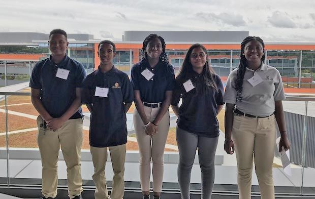The five Cristo Rey students standing on a balcony at MathWorks. Behind them is the company campus including other MathWorks buildings.