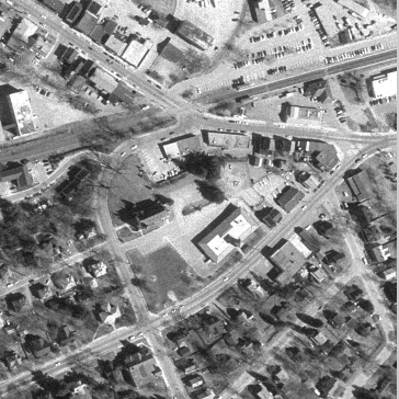 Grayscale photo of the same roads and buildings as seen from a different point in the sky. The scene is rotated, translated, and tilted with respect to the aerial photo.